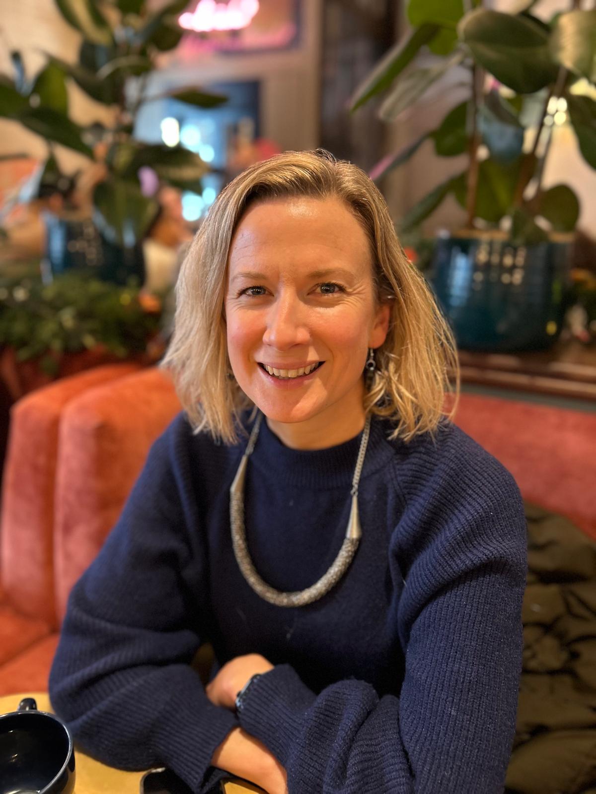 Portrait of the workshop tutor, smiling in a cosy, bookish setting.